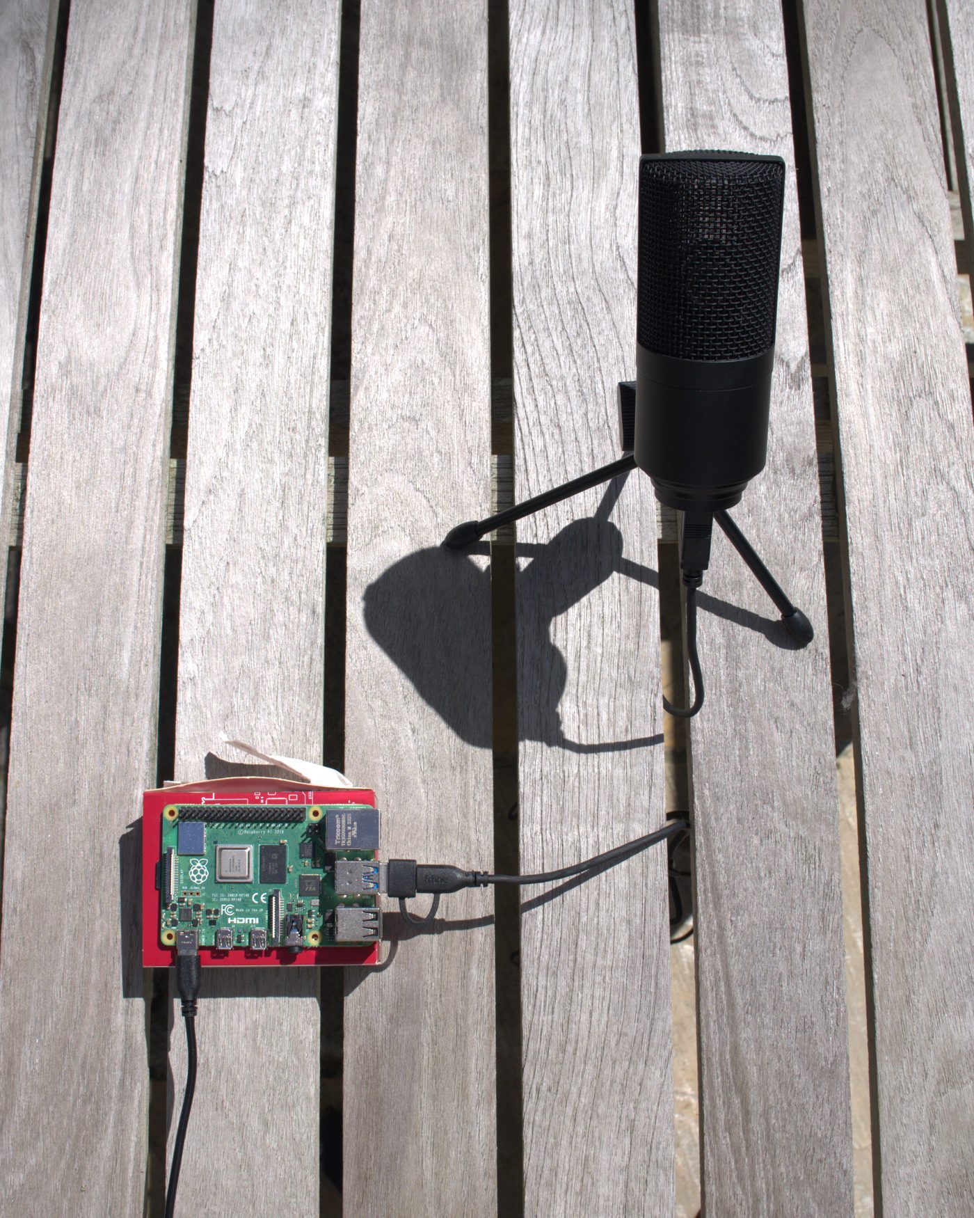 The first HeliTracker unit on a wooden deck: a Raspberry Pi in a red case wired to a USB microphone on a small tripod
